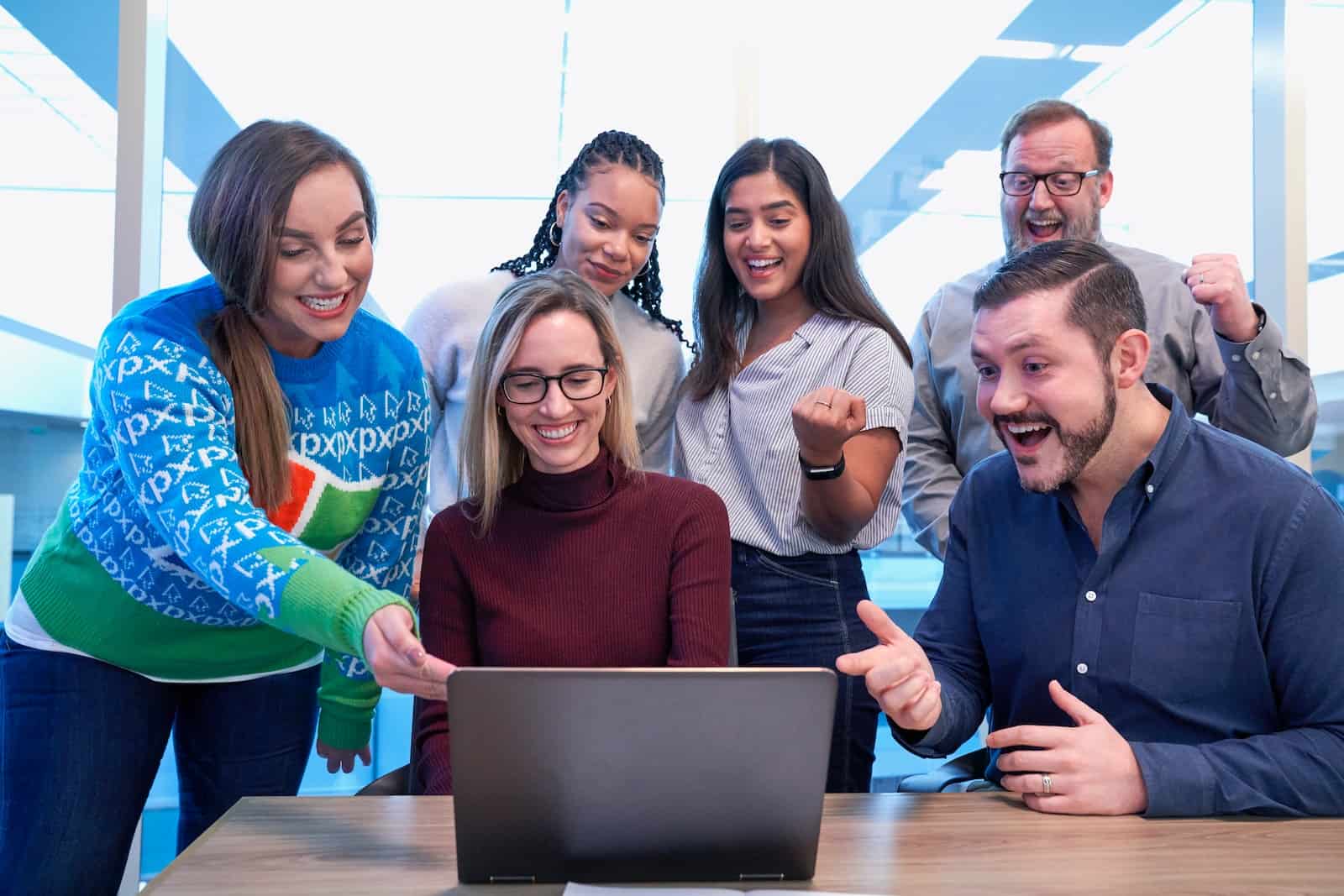 men and women sitting and standing while staring at laptop